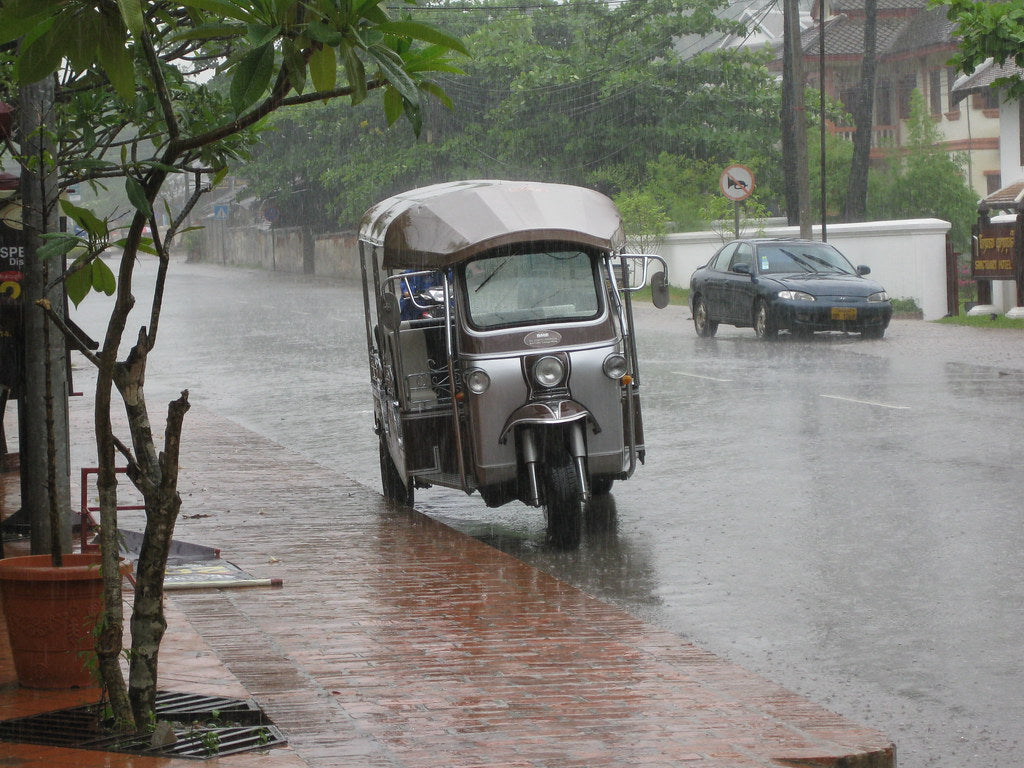A tuk-tuk parked on a rain-soaked street during a tropical downpour